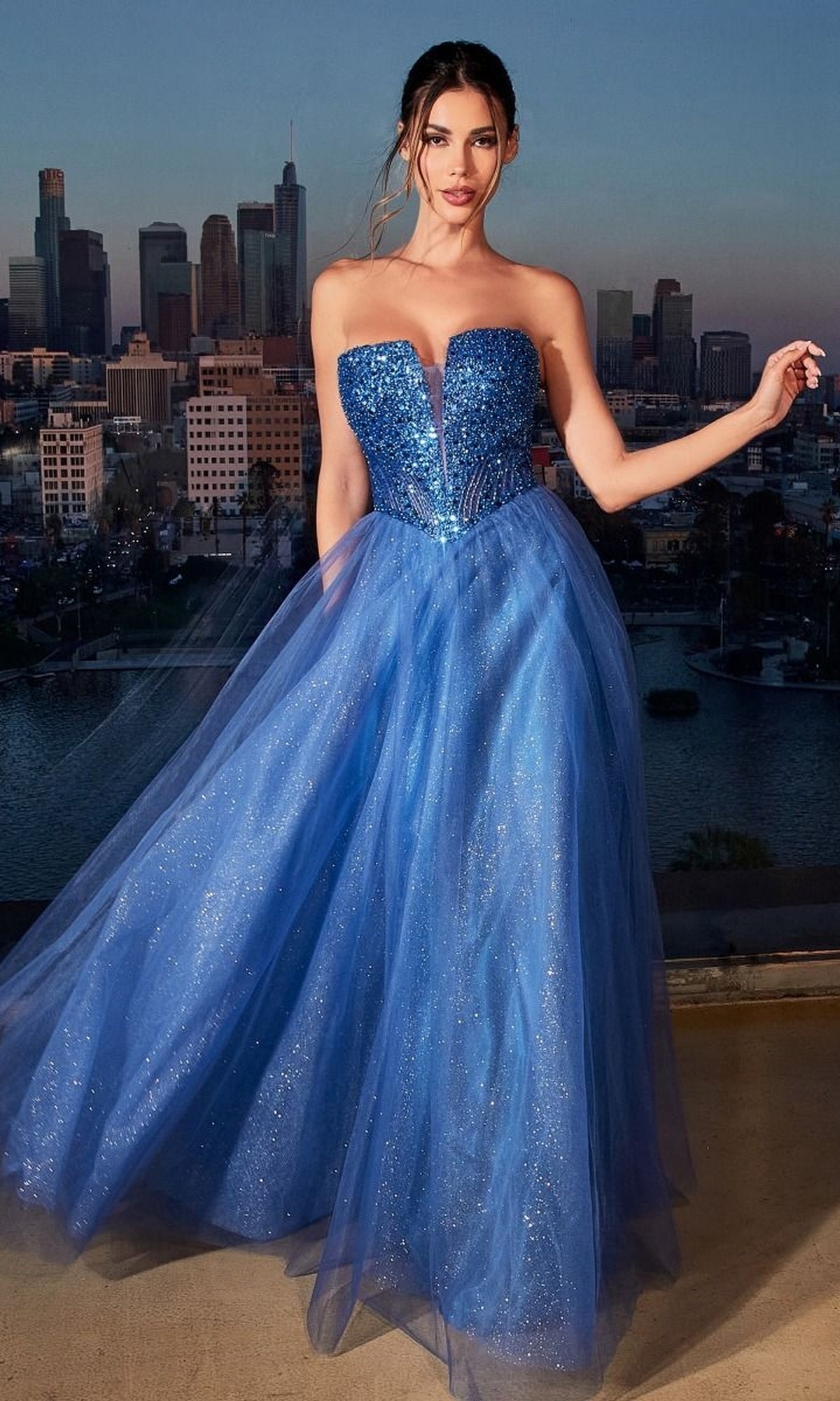 A woman stands outdoors at dusk in a Lace-Up Strapless Long Glitter Prom Dress CD0217, her sparkling blue gown shimmering against the city skyline.